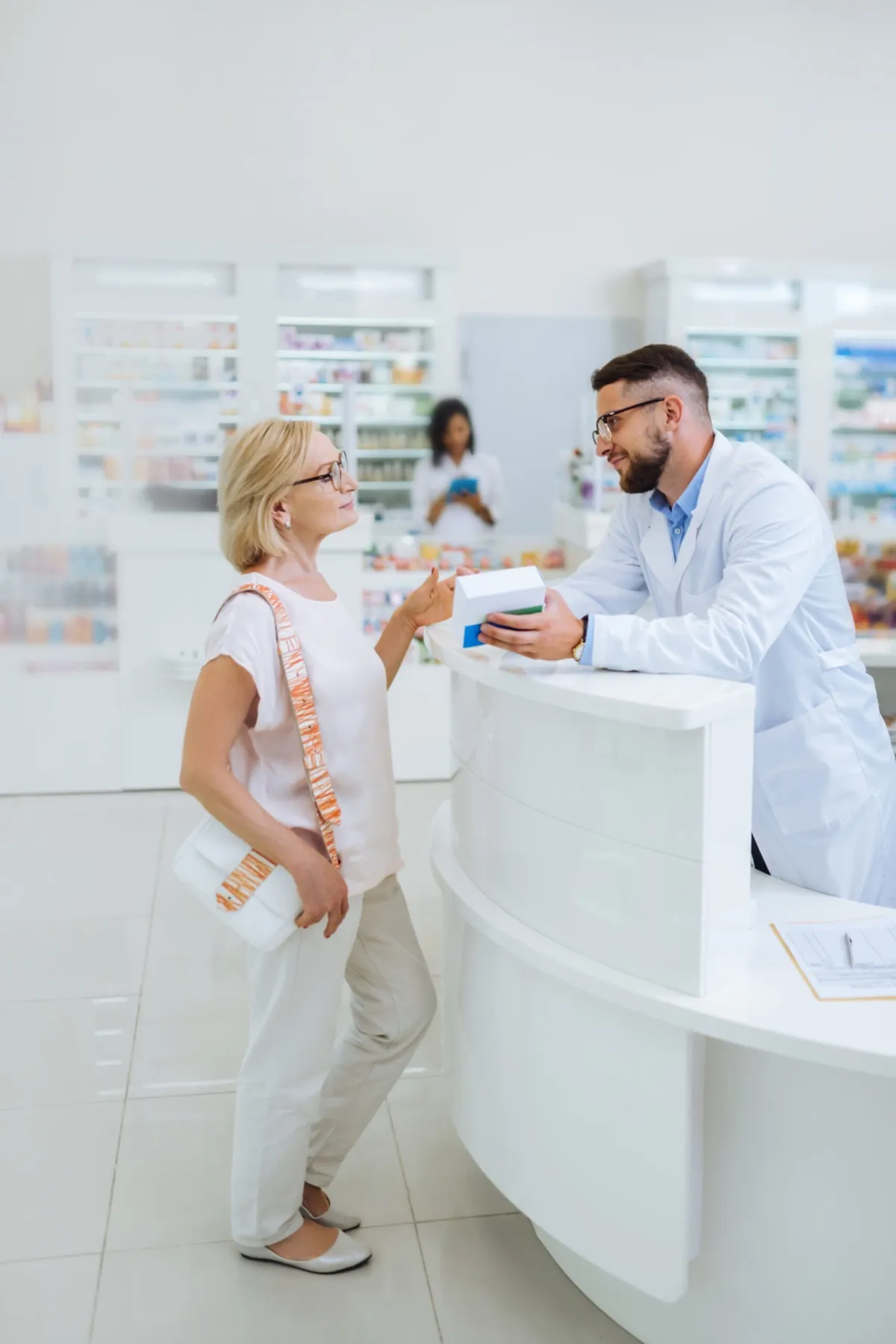An older woman asks a pharmacist about her medicine at a bright pharmacy counter